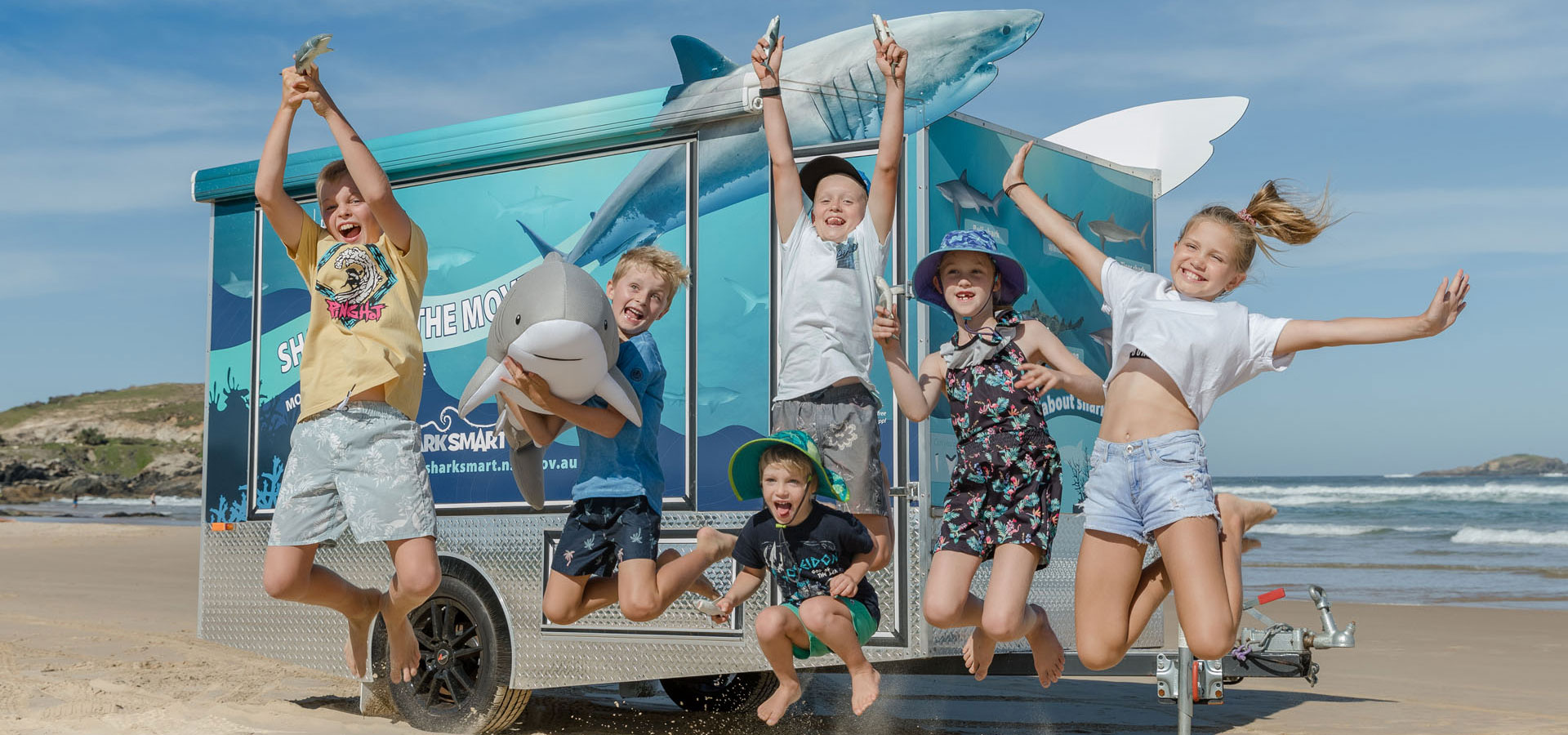 Kids are jumping with joy in front of the shark trailer